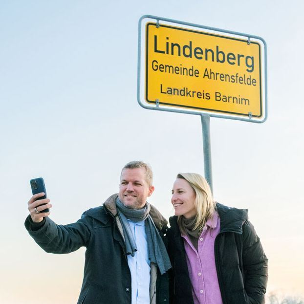 Moritz Cassalette und Christina Hollstein stehen vor einem Mikrofon im Studio und lächeln.